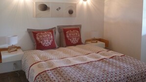 Ein Schlafzimmer mit Holzbalkendecke, zwei Nachttischlampen, einem Bett mit gemustertem Überwurf und einem Nachttisch mit Lampe.