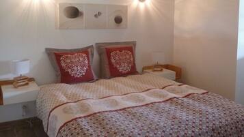 Une chambre à coucher avec un plafond en bois, deux lampes de chevet, un lit recouvert d’une couvre-lit à motifs et une table de chevet avec une lampe.