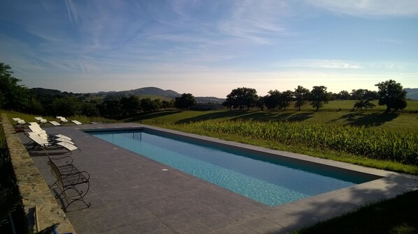 A rectangular swimming pool with a tiled deck and lounge chairs along one side.
