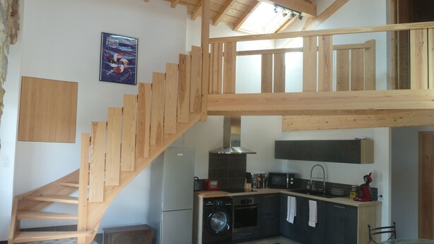 Eine geräumige Küche mit einer Holztreppe, die in einen oberen Bereich führt, einer Waschmaschine und einem Fliesenboden.