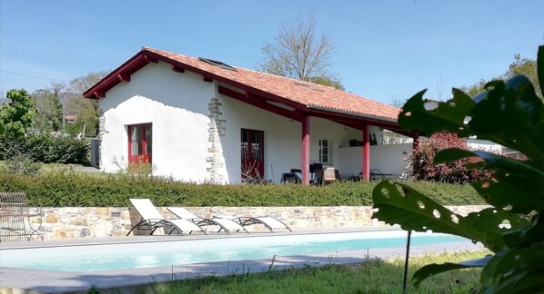 A white building with a red roof and stone walls, a pool, and a patio area. - Charming gîte with swimming pool and mountain views in the heart of the Basque Country (Ossès)