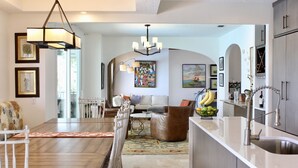 A modern kitchen with a central island, a dining area with a wooden table and chairs, and a living room with a sofa and a coffee table. - Luxury  Villa with heated pool, spa/hot tub, dock, near beach,  Sunsets! (St. Augustine)