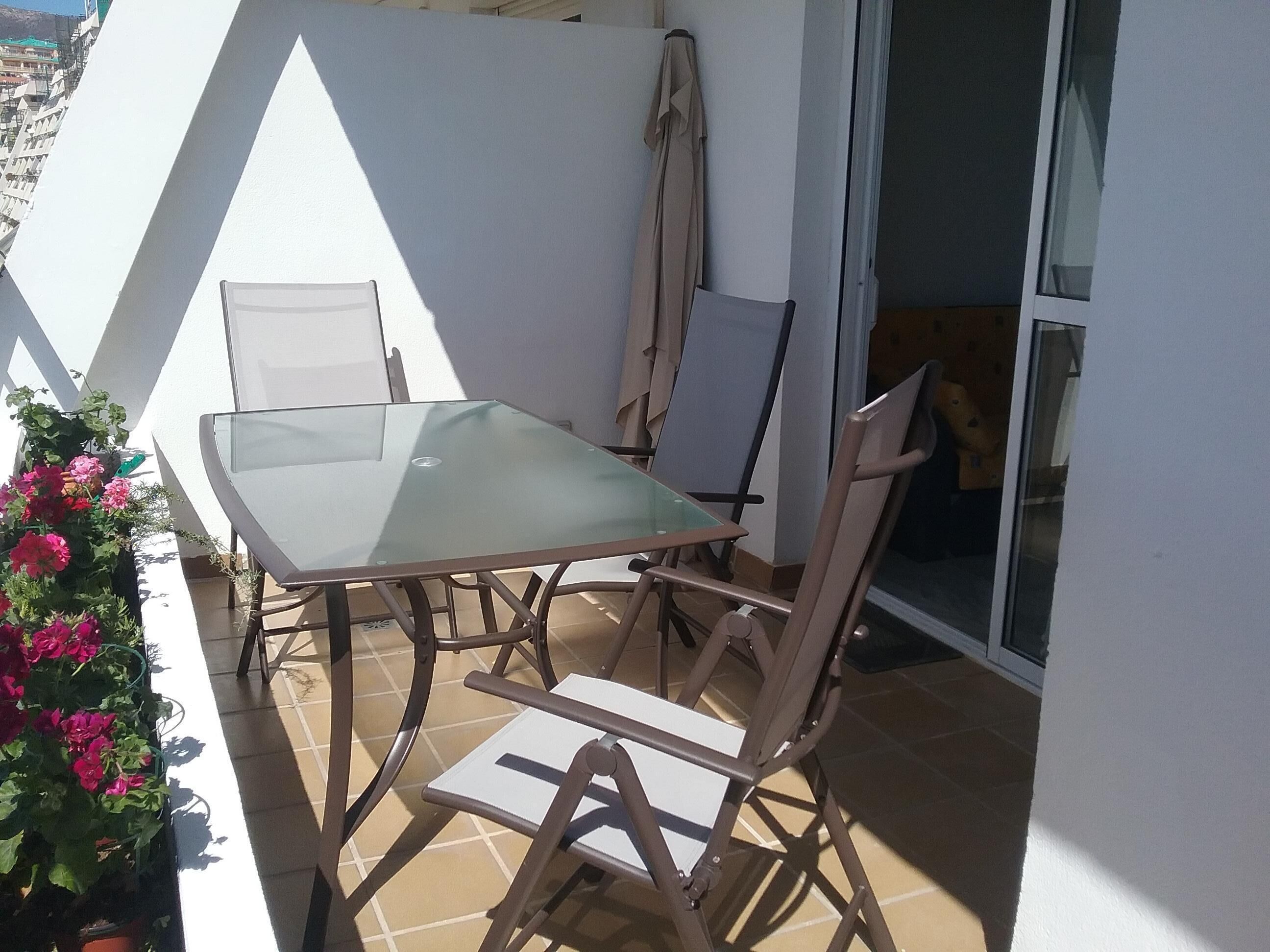 Un pequeño patio al aire libre con una mesa de vidrio y cuatro sillas.