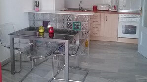 Een moderne keuken met een eethoek, met een glazen tafel, stoelen, een plafondventilator en een inbouwoven.