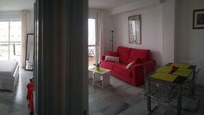 Een kamer met een bed, een rode bank, een tafeltje en een stoel.