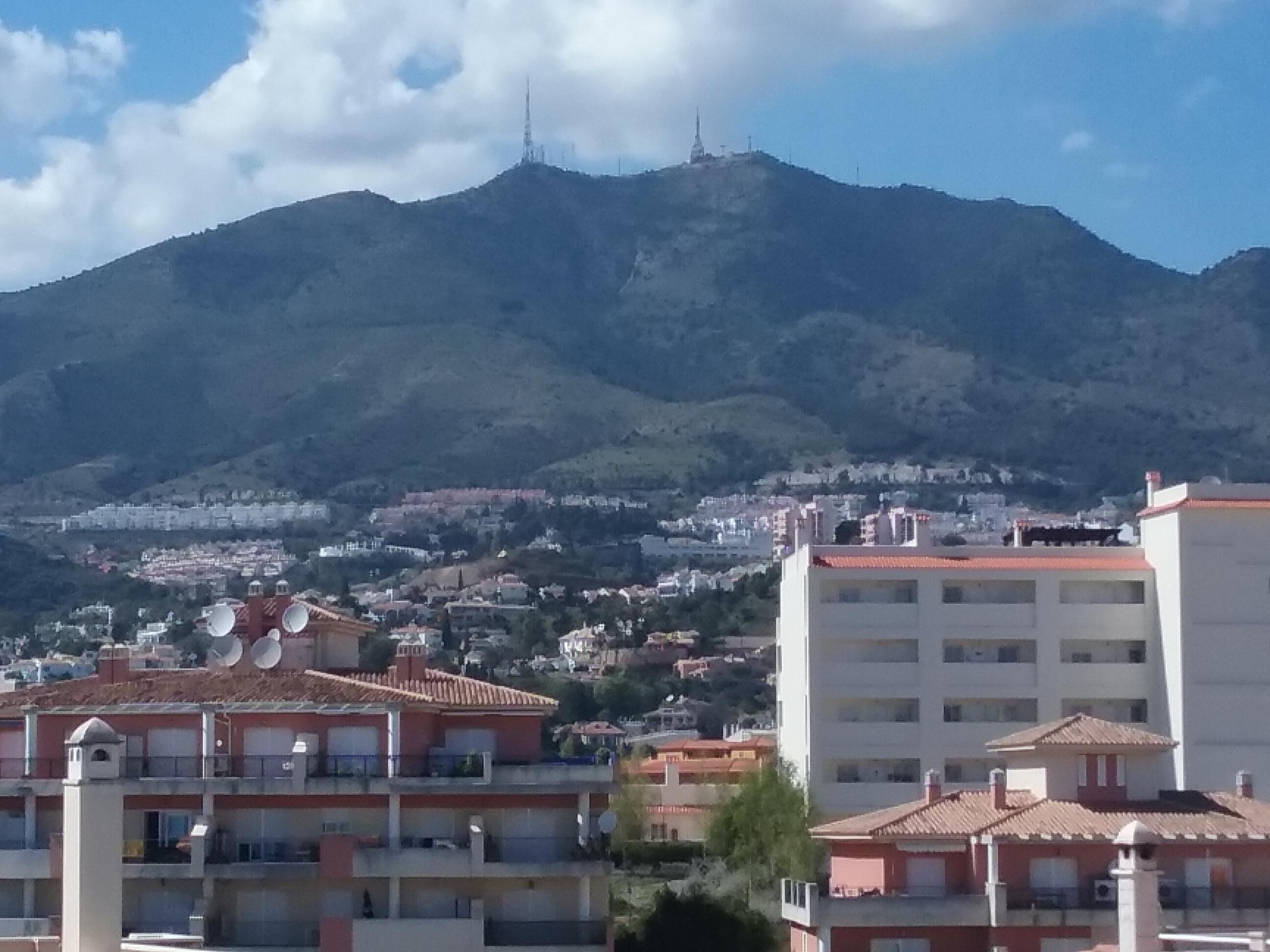 A residential area with buildings, a mountain in the background, and a clear sky.