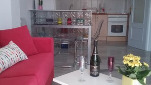 Een moderne woonkamer met een rode bank en een witte salontafel. Achtergrond toont een keuken met witte kasten, een fornuis en een spoelbak.