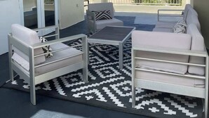 A balcony with a sofa, a chair, and a small table. There is a view of the ocean and other buildings in the background.