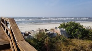 Een houten looppad dat naar een strand leidt, met golven die op de kust breken.