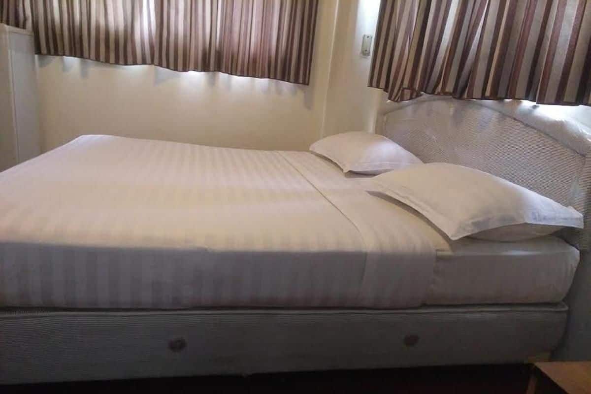A single bed with a white mattress and pillows, a headboard, and curtains on the windows.