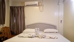 A hotel room with a bed, a wooden chair, a window with curtains, and an air conditioning unit.