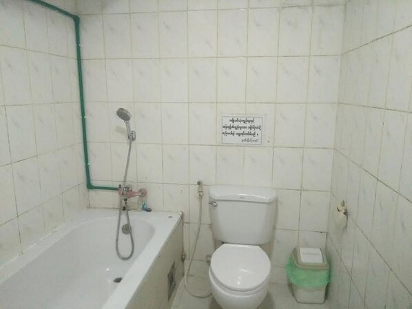A small bathroom with a bathtub, toilet, and a green trash bin.