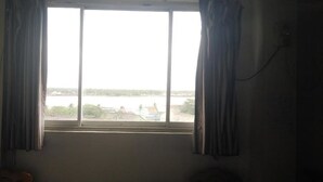 A room with a large window, curtains, and a view of a body of water and buildings.