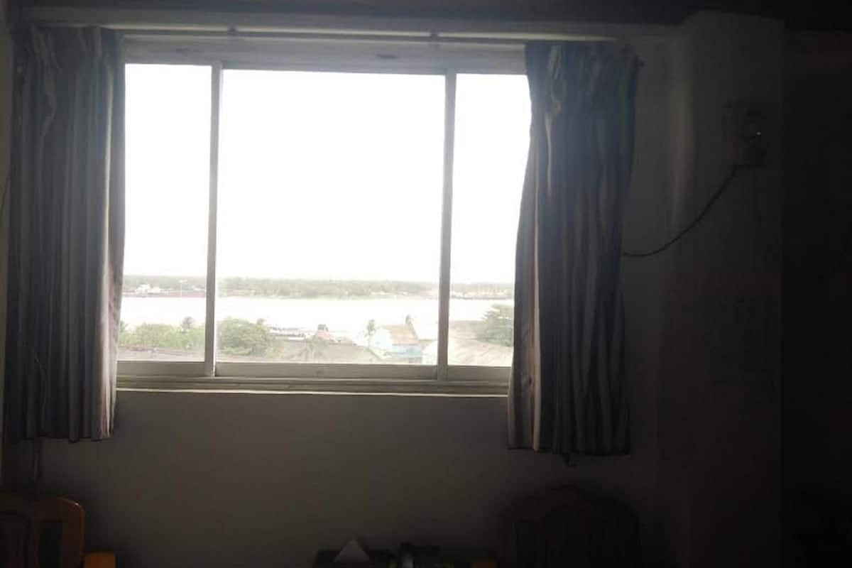 A room with a large window, curtains, and a view of a body of water and buildings.