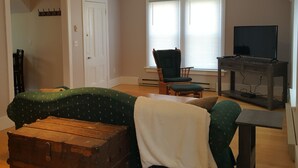 A living room with a green sofa, a wooden chest, a television on a stand, and a chair. - Right in the Quaint Village of Hammondsport (Hammondsport)