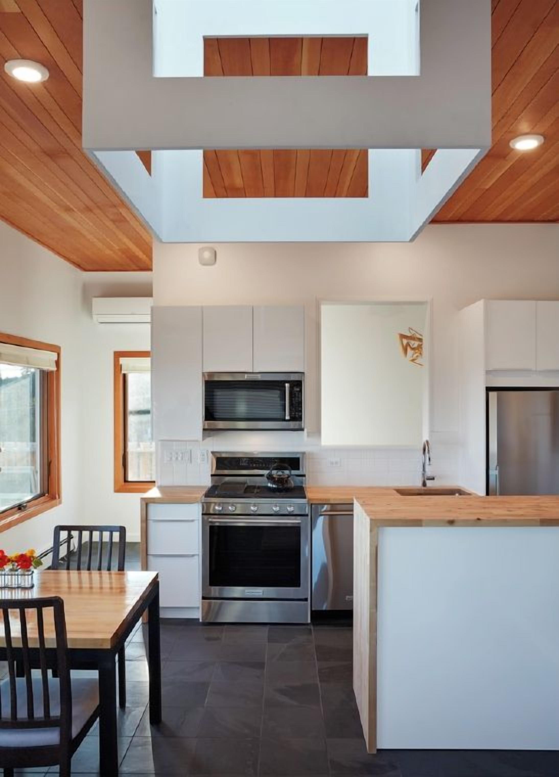 A modern kitchen with white cabinets, a stainless steel stove, and a wooden ceiling.