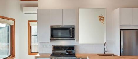 A modern kitchen with white cabinets, a stainless steel stove, and a wooden ceiling.