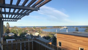 A view from a balcony overlooking a waterfront area with buildings, a boat, and a clear sky. - The SkyHouse- Life as Art- Sauna Available (Grand Marais)