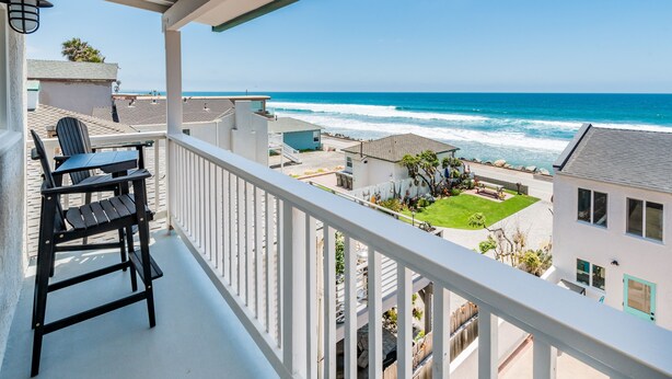 A balcony with a view of the ocean, a small table, and a chair.