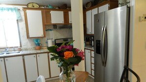 Una cocina con un refrigerador de acero inoxidable, gabinetes de madera, un florero con flores en la encimera y una ventana con cortina.