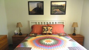 Una cama con un colcha colorida, dos almohadas y dos mesitas de noche con lámparas.