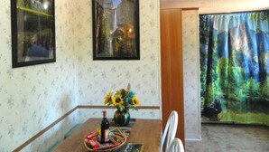 Un comedor con papel tapiz floral, dos cuadros enmarcados, un jarrón con girasoles y una mesa con una botella y aperitivos.