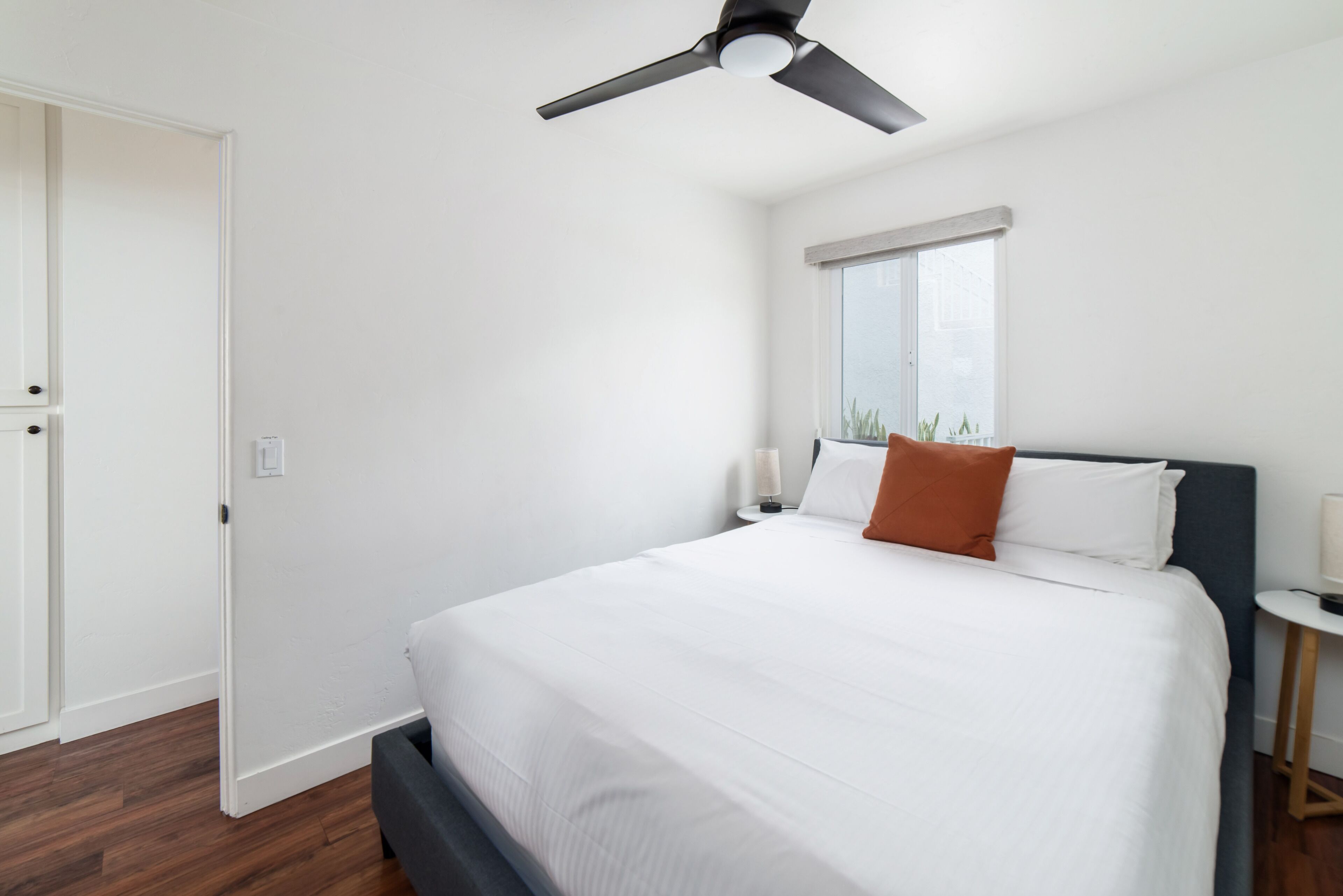 Une chambre à coucher avec un lit, un ventilateur de plafond, une fenêtre et une table de chevet.