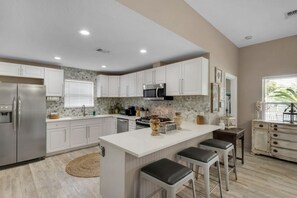 A modern kitchen with white cabinets, stainless steel appliances, a central island with bar stools, and a decorative backsplash.