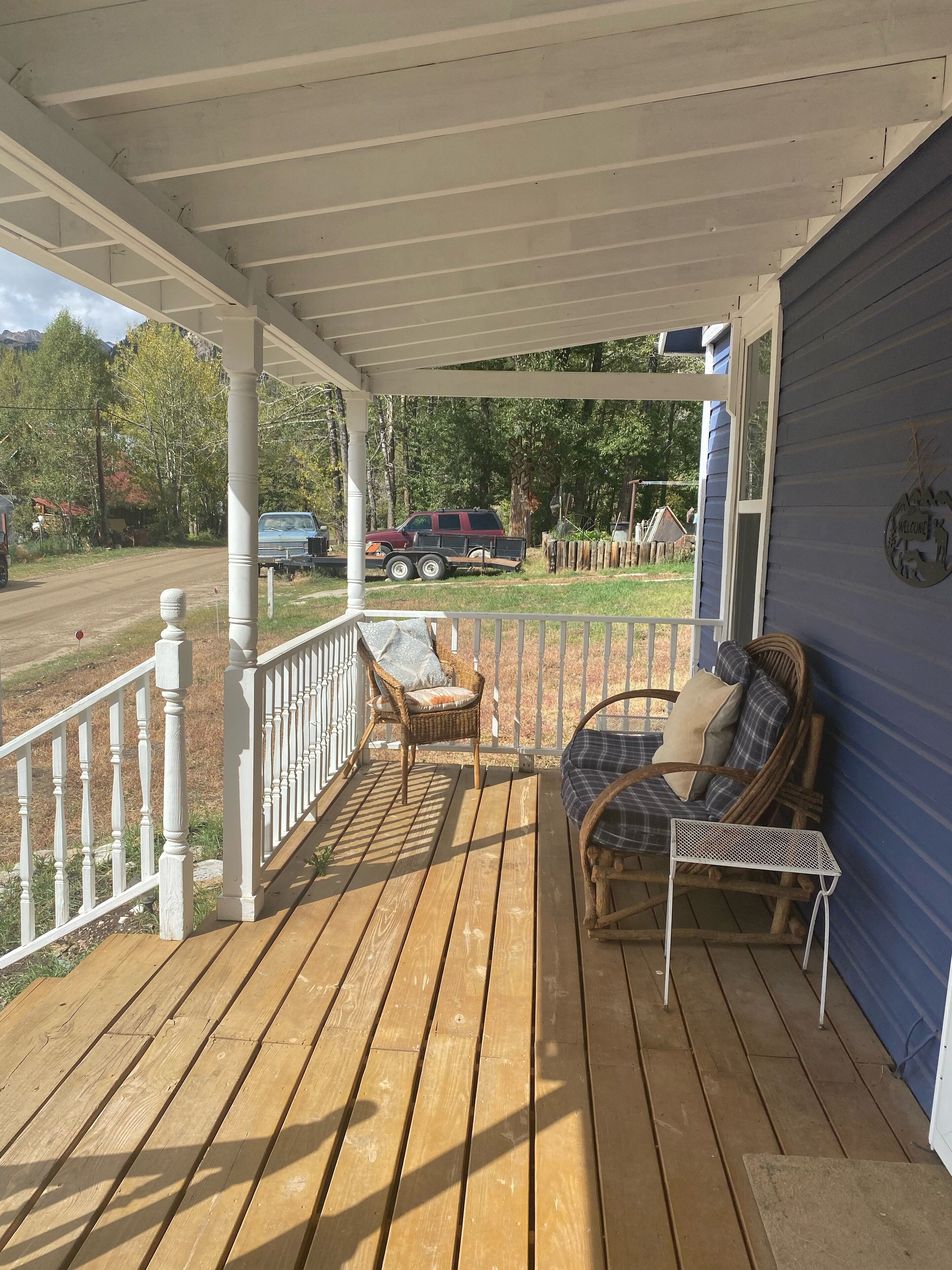 Une terrasse en bois avec un porche abrité, deux fauteuils en osier et un banc.