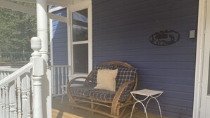 A porch with a wicker chair and a small table, a white railing, and a window.