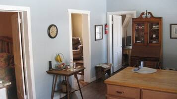 A room with a wooden table, a chair, a clock on the wall, and a cabinet with glass doors.