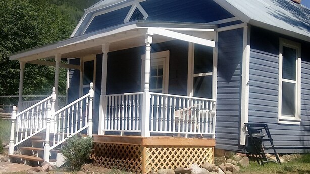 A single-story house with a porch, a chimney, and a view of a hill.