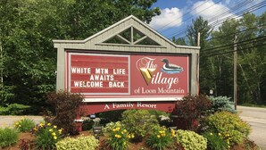 Naamplaatje voor The Village of Loon Mountain, een gezinsresort, met een gastvrije boodschap en een afbeelding van een loon.