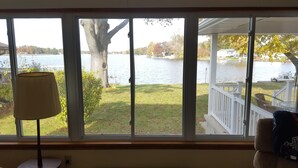 A room with a large window overlooking a lake, a lamp, and a chair.