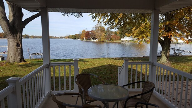 A covered outdoor seating area with a view of a lake and houses in the background.