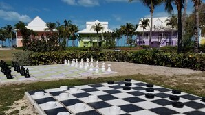 A large outdoor chessboard set up in a garden with palm trees and colorful buildings in the background. - Amazing Old Bahama Bay condo perfect for you! (West End Bahamas)