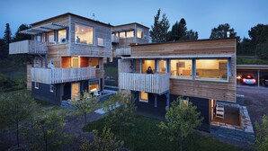 A modern multi-story house with wooden exterior and balconies, featuring large windows and a driveway. - The Aurora- Award Winning- Sauna available (Grand Marais)