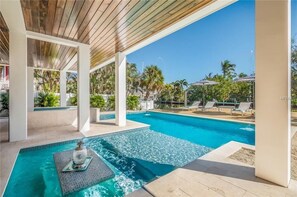Una piscina con una pérgola superior, rodeada de palmeras y sillas de descanso.