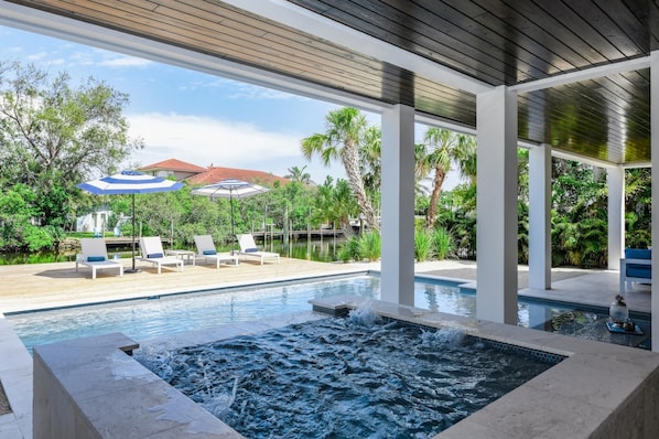Un espace piscine comprenant un jacuzzi, des chaises longues et des parasols.