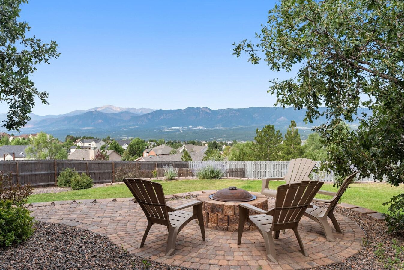 A patio with two Adirondack chairs, a round table, and a fire pit.
