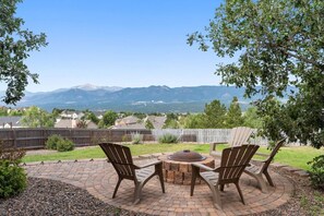 Une terrasse avec deux fauteuils Adirondack, une table ronde et un foyer extérieur.
