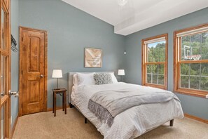 Une chambre avec un lit, deux lampes de chevet, une porte en bois, une citation encadrée au mur et une fenêtre donnant sur un panier de basketball à l’extérieur.