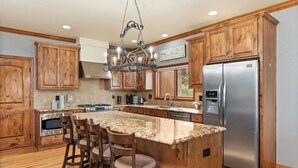Una cocina con armarios de madera, encimera de granito, refrigerador de acero inoxidable y una zona de asientos con taburetes de bar.