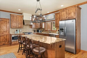 A kitchen with wooden cabinets, a granite countertop, a stainless steel refrigerator, and a bar stool seating area.