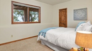 Un dormitorio con una cama grande, una ventana que da a árboles, una puerta de madera y una obra de arte colgada en la pared.