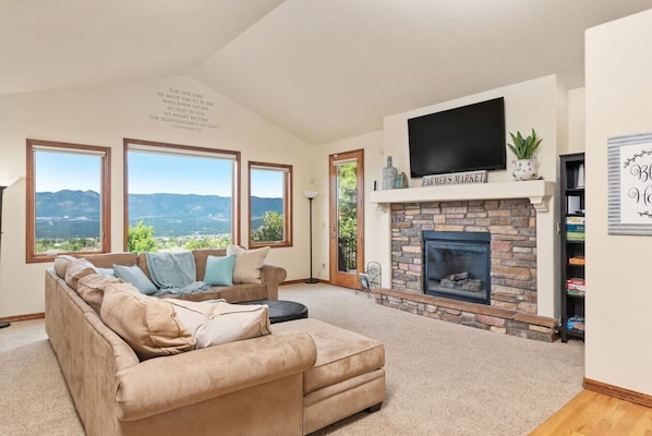Una sala de estar con un sofá seccional color beige, una chimenea y un ventanal con vistas a la montaña.