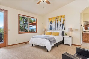 A bedroom with a bed, a nightstand, a window with a view, and a painting on the wall.