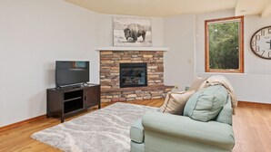 Una sala de estar con chimenea de piedra, un televisor sobre un mueble bajo, un sofá y un reloj en la pared.