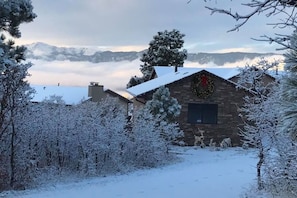 Un chalet rustique aux murs de pierre, entouré d’arbres couverts de neige et offrant une vue dégagée sur les montagnes lointaines.