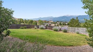 Un patio trasero con valla de madera, césped y vista a casas y montañas al fondo.